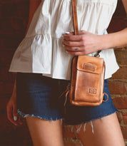 A woman in denim shorts holding a Bed Stu Alelike premium leather crossbody bag.