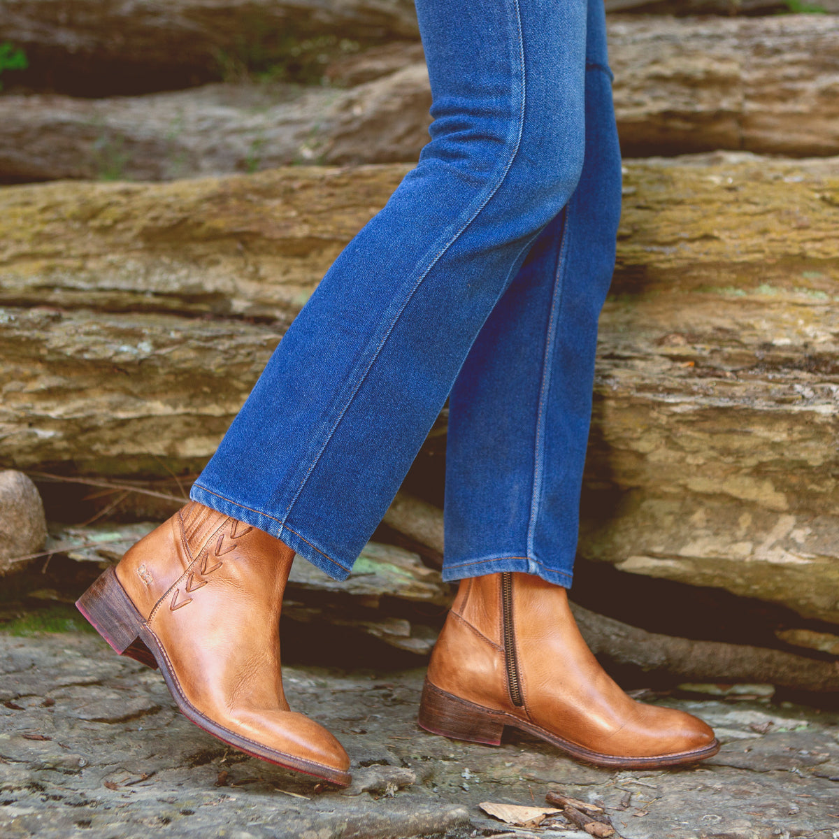 A woman wearing Bed Stu Alina denim jeans and Bed Stu leather ankle boots standing on a rock.