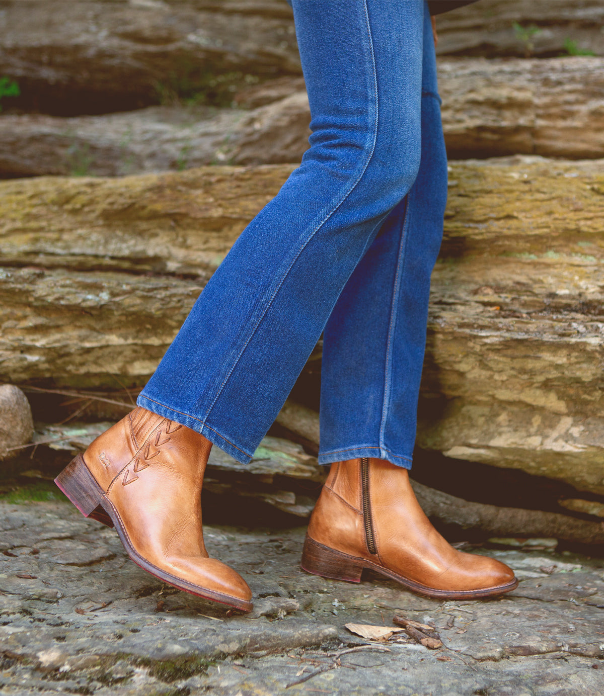 A woman wearing Bed Stu Alina denim jeans and Bed Stu leather ankle boots standing on a rock.