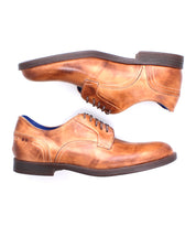 The Bed Stu Anchiano features a classic oxford-style lace-up design in brown leather with dark soles, shown side view—one shoe facing left, the other right.
