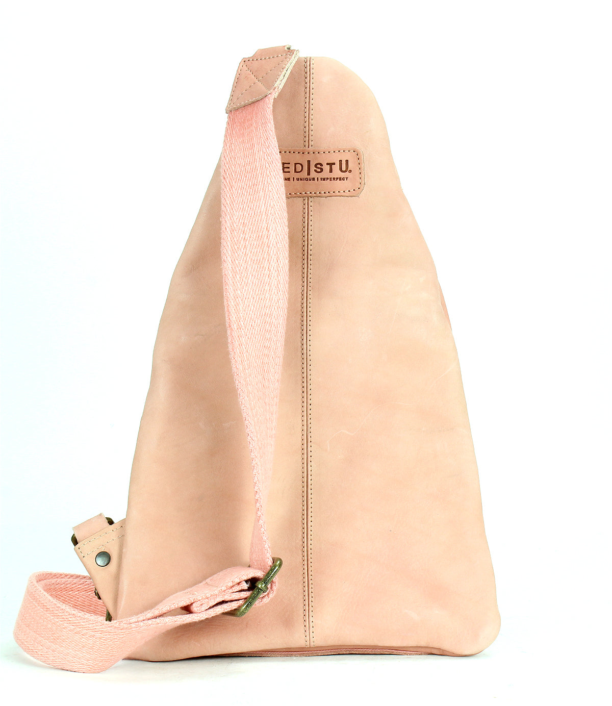 The Andie sling bag by Bed Stu features beige leather with a single pink adjustable strap and a stitched logo tag on top, presenting a versatile accessory against a white background.