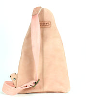 The Andie sling bag by Bed Stu features beige leather with a single pink adjustable strap and a stitched logo tag on top, presenting a versatile accessory against a white background.