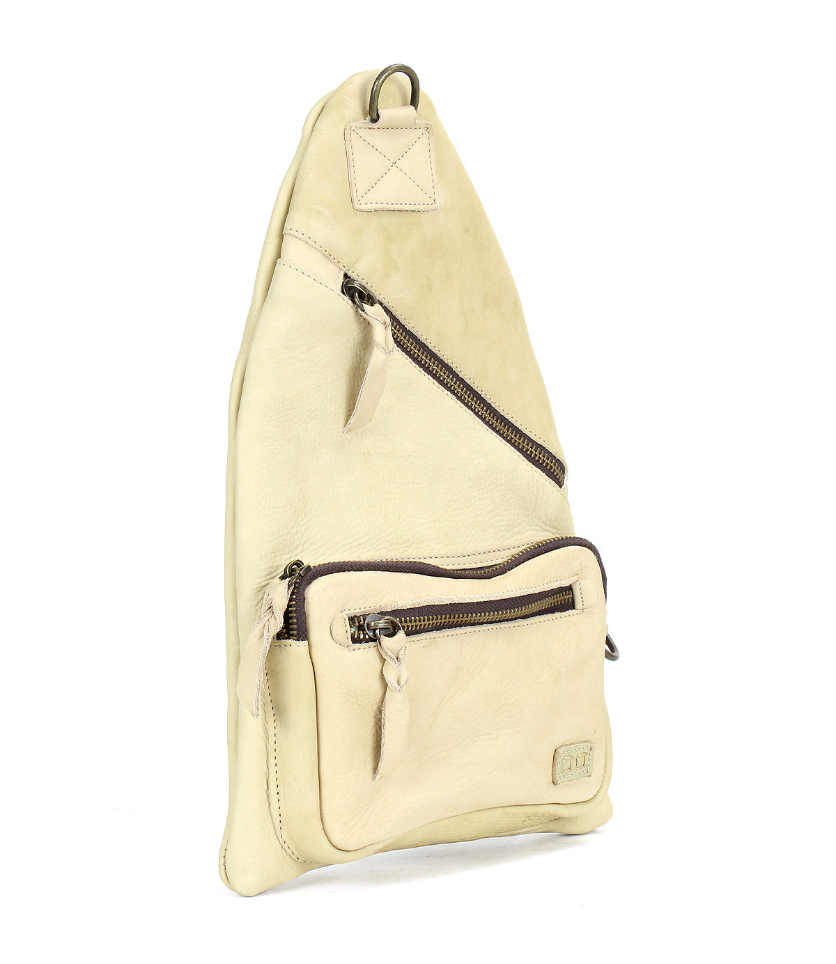 The Andie by Bed Stu is a versatile beige leather crossbody sling bag with two zippered compartments and a sleek metal ring at the top, offering practical style for any occasion.