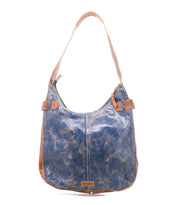 The Bed Stu Argus is a blue and brown handcrafted leather shoulder bag featuring a single wide strap, prominent stitching, oversized front pockets, and a weathered finish, shown against a white background.