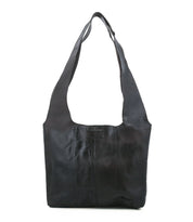 The Ariel Mid by Bed Stu is a black artisanal leather bag with wide straps, a rectangular shape, visible stitching, magnetic closure, and an embossed logo patch on the front—ideal for everyday use.