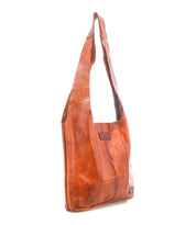 The Bed Stu Ariel Mid is a brown full-grain leather shoulder bag with a wide strap and visible stitching, shown upright on a white background.