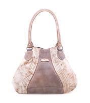 The Bed Stu Astana is a modern beige and taupe handbag featuring two handles, decorative stitching, and a metallic logo on the lower right corner, displayed against a white background.