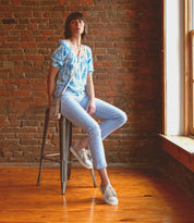 A stylish woman sitting comfortably on a Bed Stu stool in front of a brick wall.