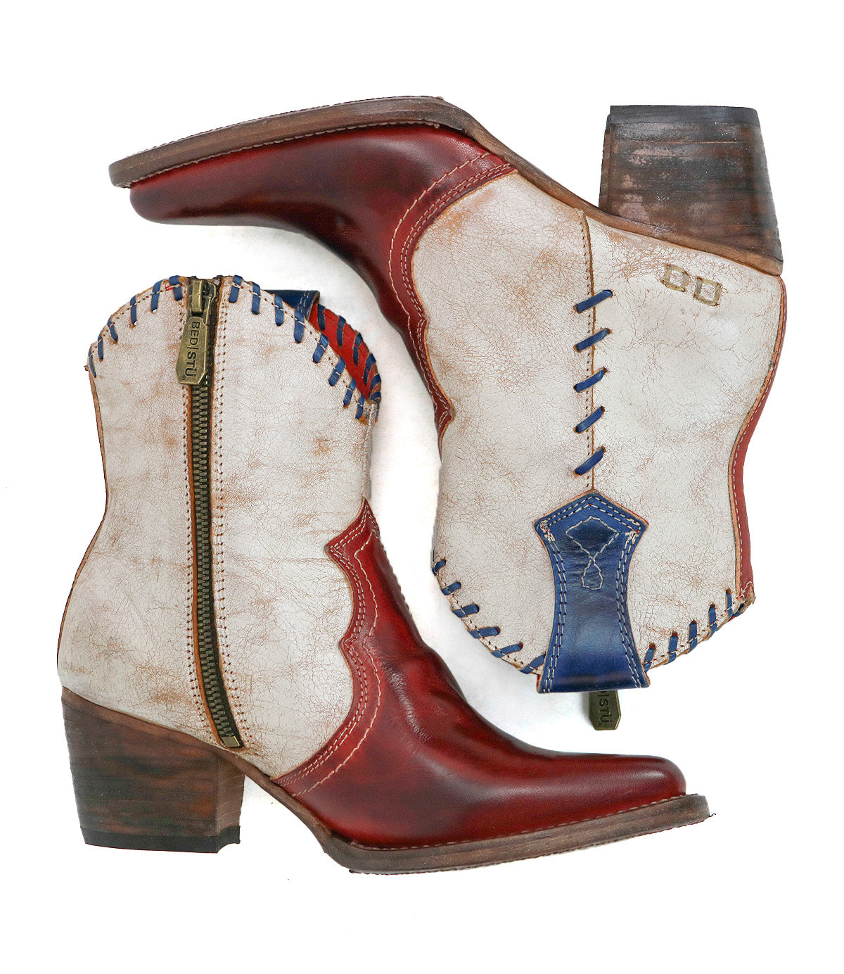 The Bed Stu Baila II is a pair of mid-calf, Western-inspired boots in red and white leather with blue stitching, pointed toe, side zippers, and chunky heels, shown on a white background.