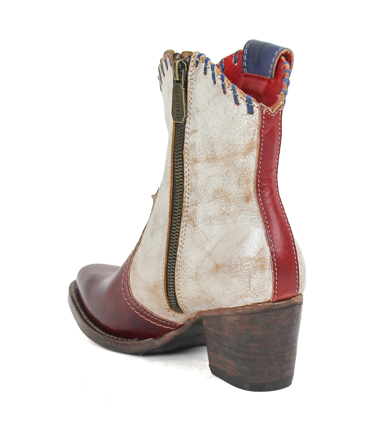 The Bed Stu Baila II is a women's ankle boot featuring a pointed toe, side zipper, red and white leather panels, blue stitching, artisanal construction, and a stacked wooden heel.