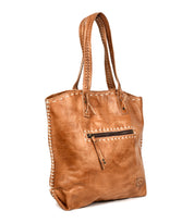 The Barra tote by Bed Stu features dual handles, eco-friendly leather finishes, contrast stitching, a front zip pocket, and decorative edge detailing.