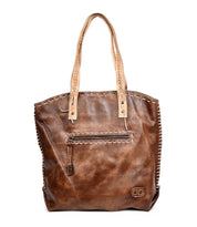 The Bed Stu Barra is a brown leather tote with tan handles, front zipper pocket, contrast stitching, and a small embossed logo at the lower right. Handmade with eco-friendly finishes for timeless, sustainable style.
