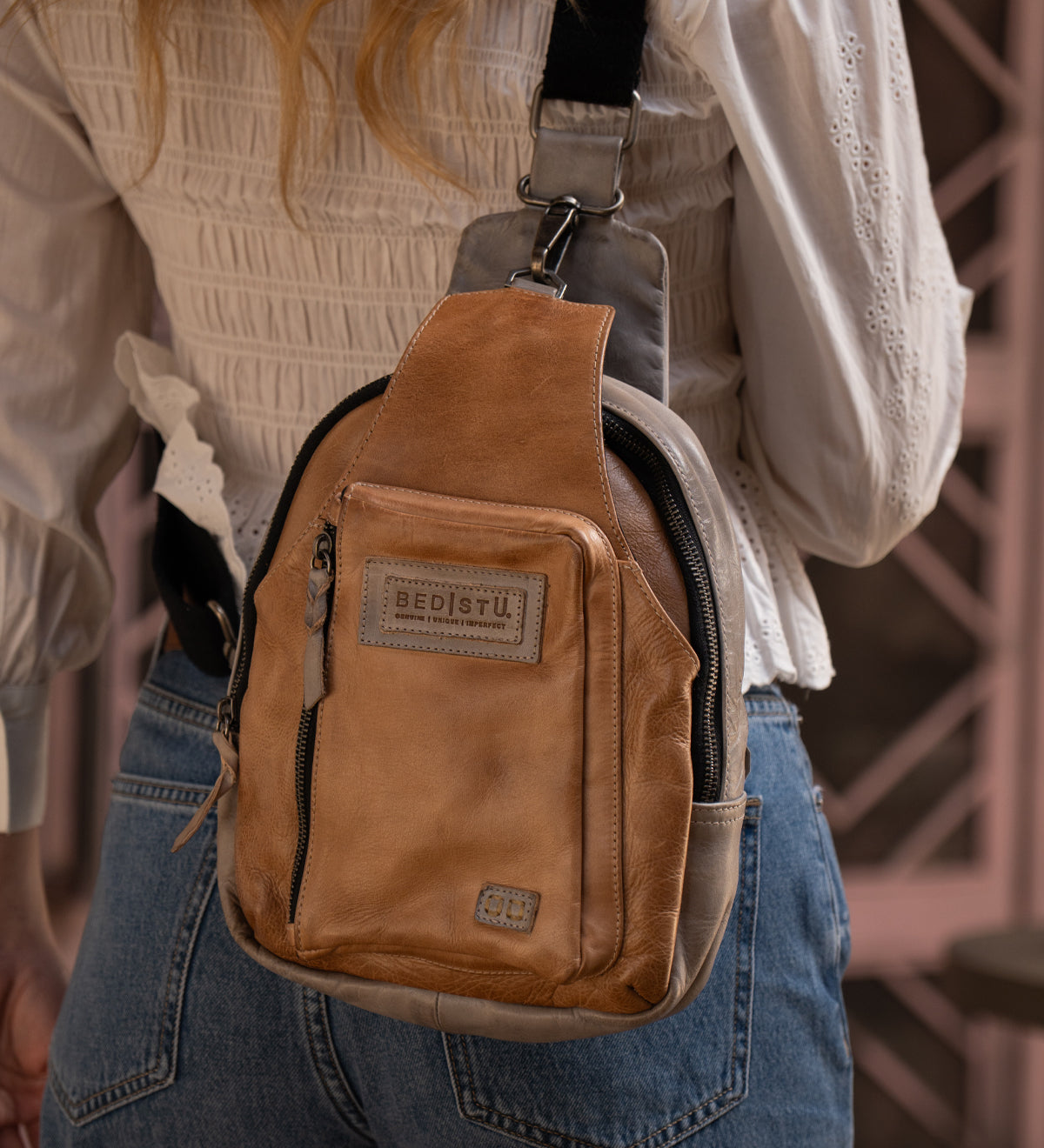 Person wearing the Bed|Stü Beau tan leather sling backpack over a white textured blouse and blue jeans, shown from the back.