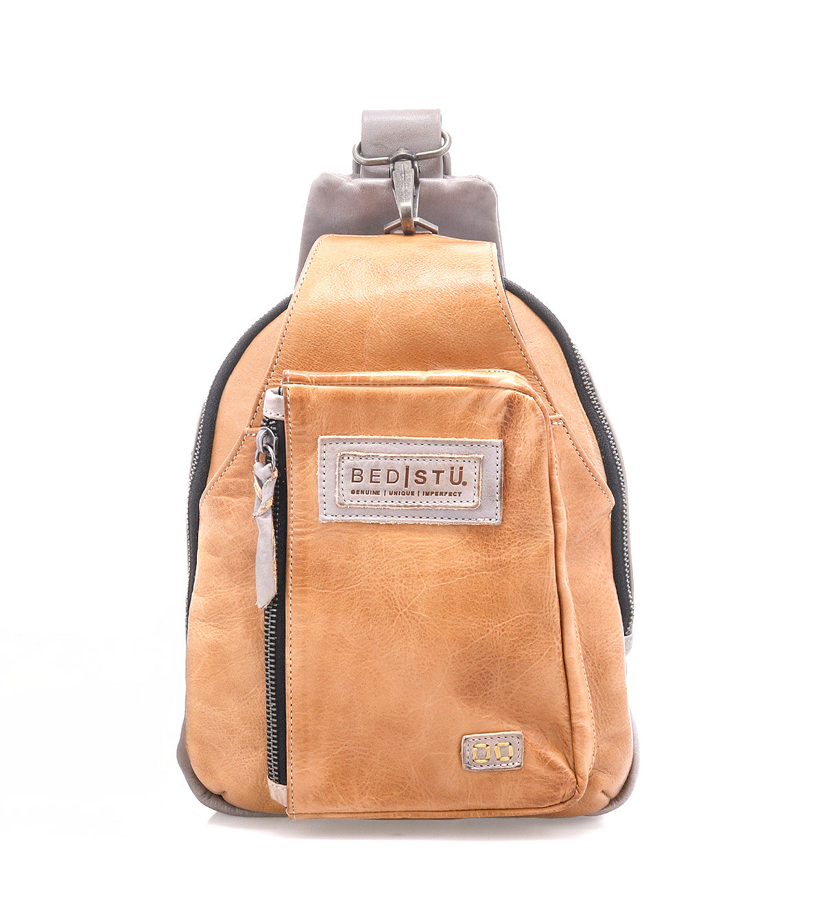 The Beau backpack by Bed|Stü is a compact tan leather sling with a front zipper pocket, signature "BED|STU" patch, and a single adjustable strap, shown against a white background.