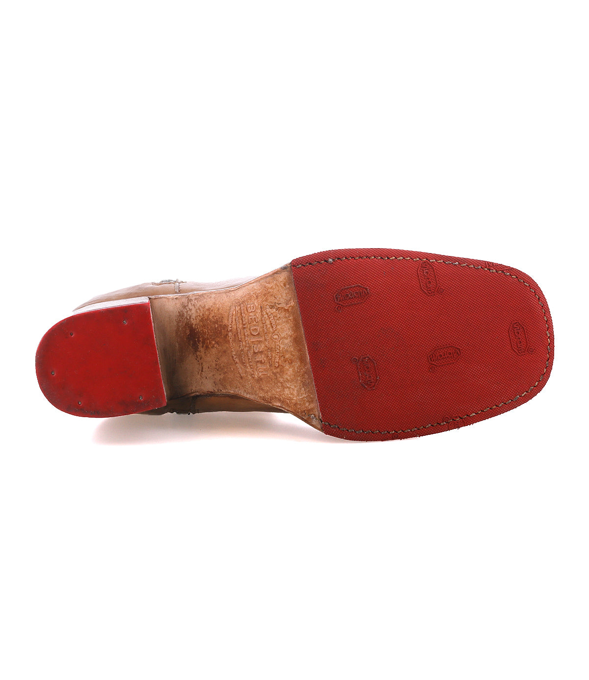 The underside of the Bed Stu Bitsy ankle boot features a hand-finished leather design, red rubber sole, stacked wooden heel, visible logos, and textured grip patterns.