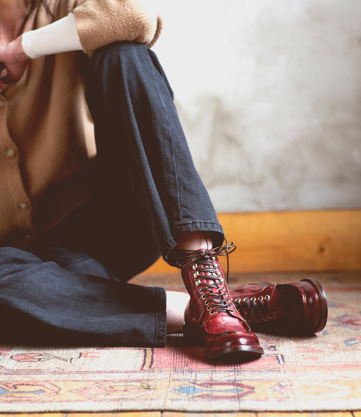 A woman sitting on a rug wearing Blimey red leather boots from Bed Stu.