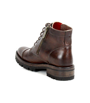 The Bed|Stü Bonnie IV is a brown leather combat boot featuring a lace-up front, dual side zippers for added convenience, sturdy treaded sole, and visible stitching. Shown from the back right angle, this sleek yet no-frills silhouette offers both durability and classic style.