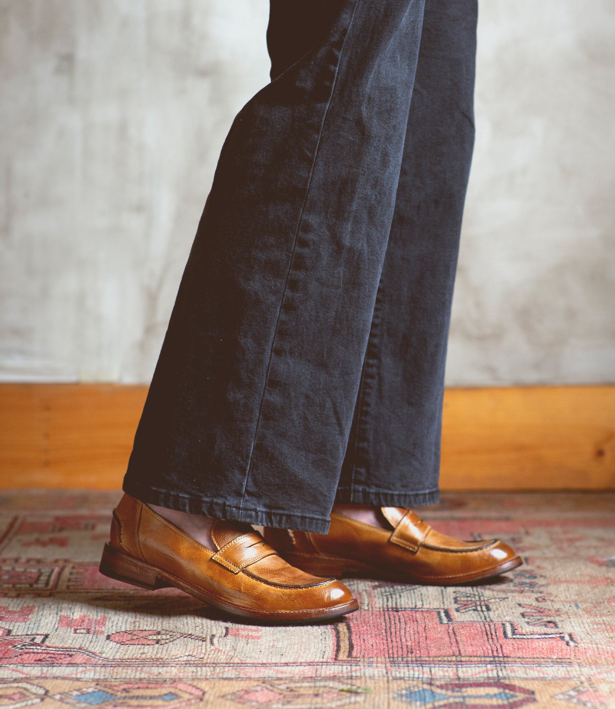 A person standing on a rug wearing a pair of Bed Stu Bonus penny loafers crafted from Italian leather.