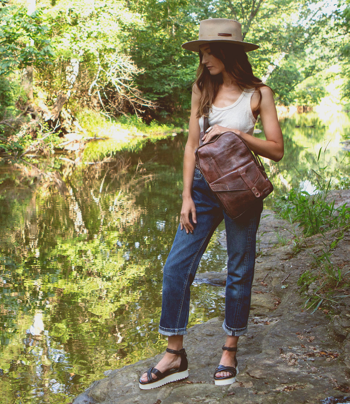 A woman wearing a Boss hat and jeans standing next to a river.