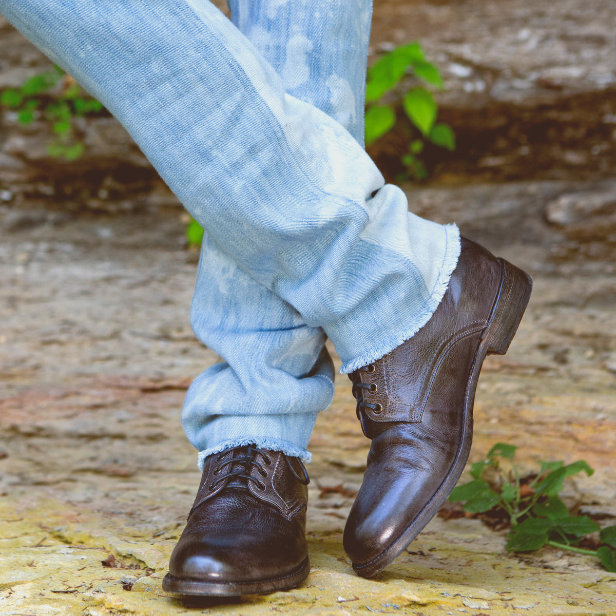Person wearing rolled-up blue jeans and Bed Stu Black Rustic Boots standing on a yellow painted curb.
