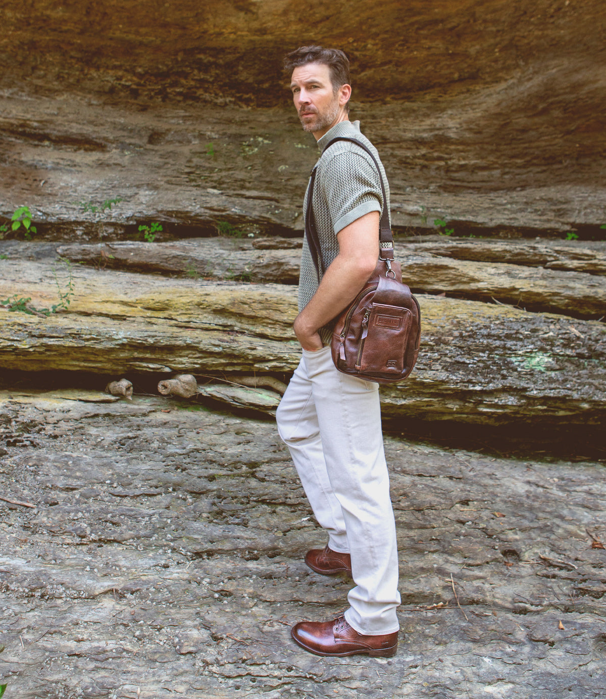 A man wearing Bed Stu leather boots stands in front of a rock formation.