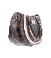 The Bed Stu Brawler is a large, worn brown leather tote bag featuring double handles, metal rings, and a versatile crossbody strap on a white background.
