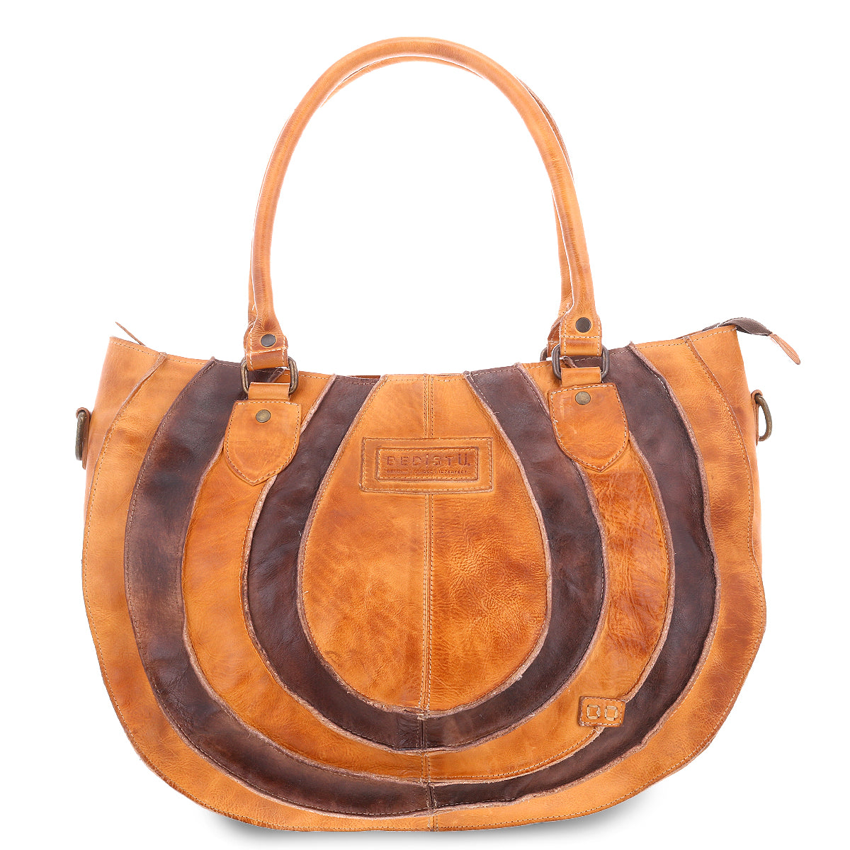 The Brawler by Bed Stu is a tan leather handbag with dark brown circular patterns, two handles, and a central rectangular label. It includes a detachable crossbody strap for versatile carrying.