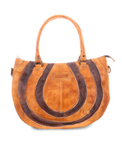 The Brawler by Bed Stu is a tan leather handbag with dark brown circular patterns, two handles, and a central rectangular label. It includes a detachable crossbody strap for versatile carrying.
