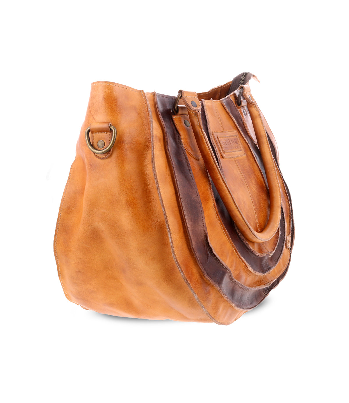 The Brawler by Bed Stu is a brown leather tote bag with a layered design. It features dual handles and has a decorative metal ring on the side.