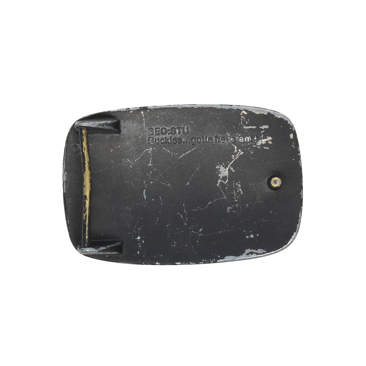 Rectangular, worn black Bed Stu 95 Buckle with visible scratches, a single screw, and "BEDSTU Buckles...gotta have 'em" engraved on its rugged metal surface.