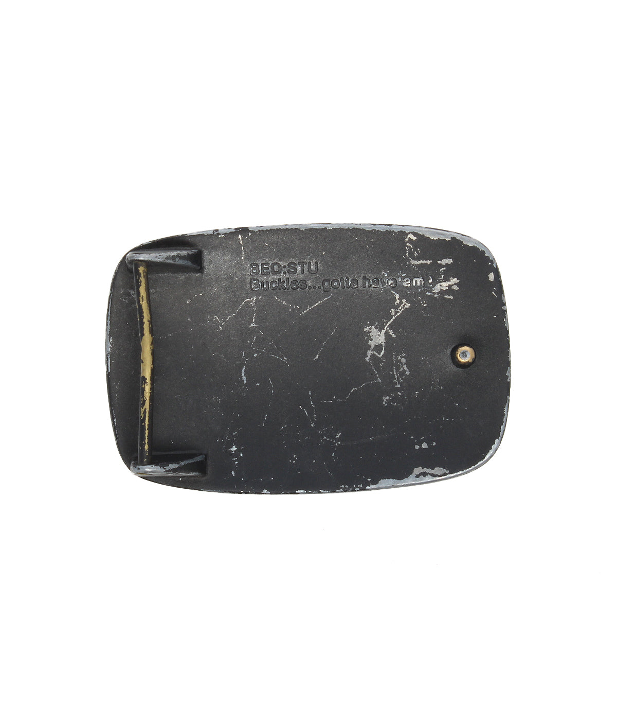 Rectangular, worn black Bed Stu 95 Buckle with visible scratches, a single screw, and "BEDSTU Buckles...gotta have 'em" engraved on its rugged metal surface.