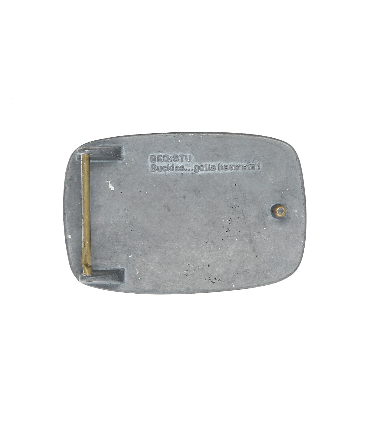 The Bed Stu 95 Buckle is a rectangular metal belt buckle featuring a brass hinge and engraved text on the back, adding rugged, distinctive style to any outfit.