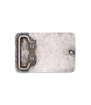 The Bed Stu Metal Cross Buckle features a rectangular vintage silver design with a raised border, small round protrusion on the right, and a metal hinge or clasp on the left side.