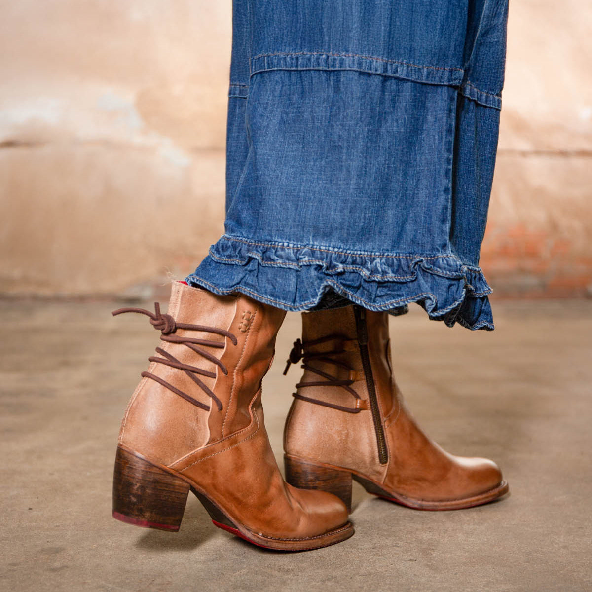 Wearing the Bed Stu Cable hand-finished leather mid-ankle boots with a Western flair and a long denim skirt, this person stands on a concrete floor.