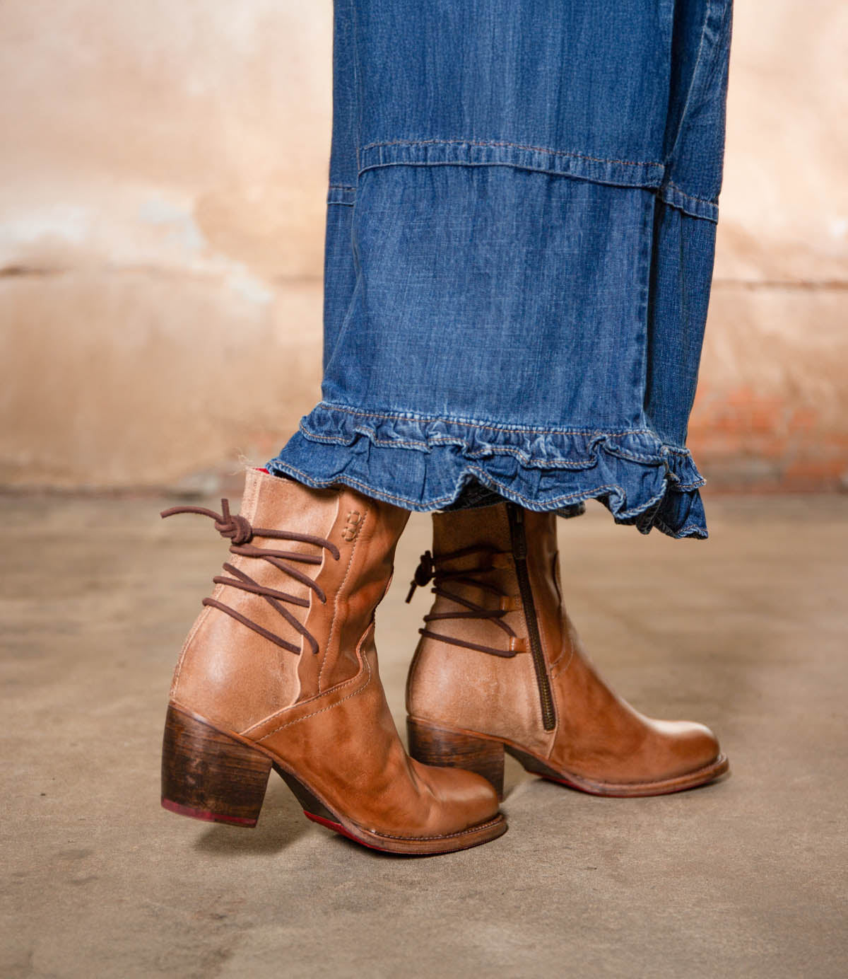 Wearing the Bed Stu Cable hand-finished leather mid-ankle boots with a Western flair and a long denim skirt, this person stands on a concrete floor.