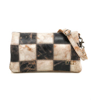 The Bed Stu Cadence PW is a rectangular crossbody bag featuring a patchwork of black and beige distressed leather squares and an adjustable strap.