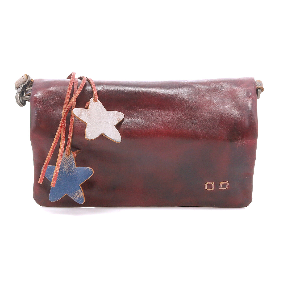 The Bed Stu Cadence is a dark brown, vegetable-tanned leather shoulder bag featuring two star-shaped leather tags—one white and one blue—attached by thin straps.