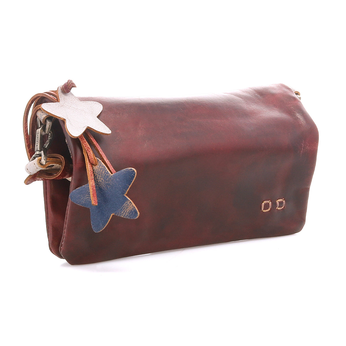 The Cadence by Bed Stu is a brown vegetable-tanned leather clutch with two star-shaped leather charms—one white, one blue—dangling from a strap attached to the zipper.