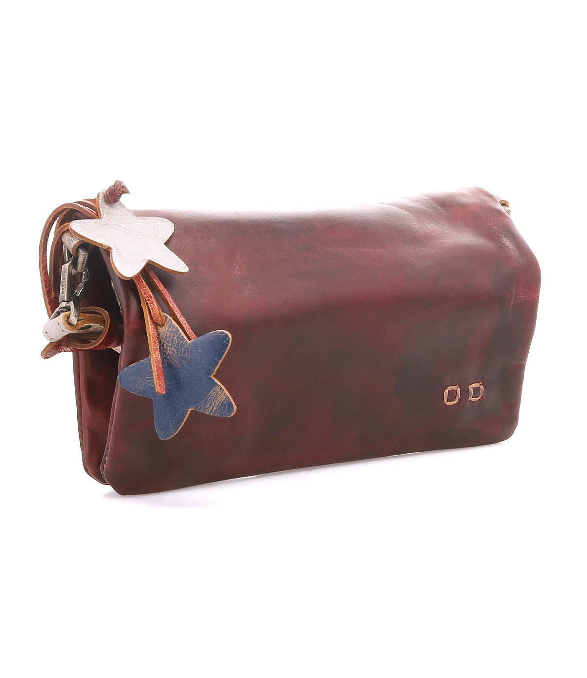 The Cadence by Bed Stu is a brown vegetable-tanned leather clutch with two star-shaped leather charms—one white, one blue—dangling from a strap attached to the zipper.