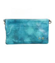 The Cadence by Bed Stu is a rectangular turquoise crossbody clutch made from textured vegetable-tanned leather, adorned with two small metallic square accents in the bottom right corner.