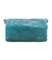 The Cadence by Bed Stu is a teal crossbody clutch made with vegetable-tanned leather, minimal stitching, and a flap closure, displayed against a white background.