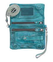 The Bed Stu Cadence is a teal crossbody clutch in vegetable-tanned leather with two front zippered pockets, transparent ID window, card slots, and detachable straps, shown laid flat and open.