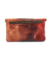 The Cadence crossbody clutch by Bed|Stü is crafted from vegetable-tanned leather in brown and red, featuring a visible front zipper pocket and a small red button detail on the left side.