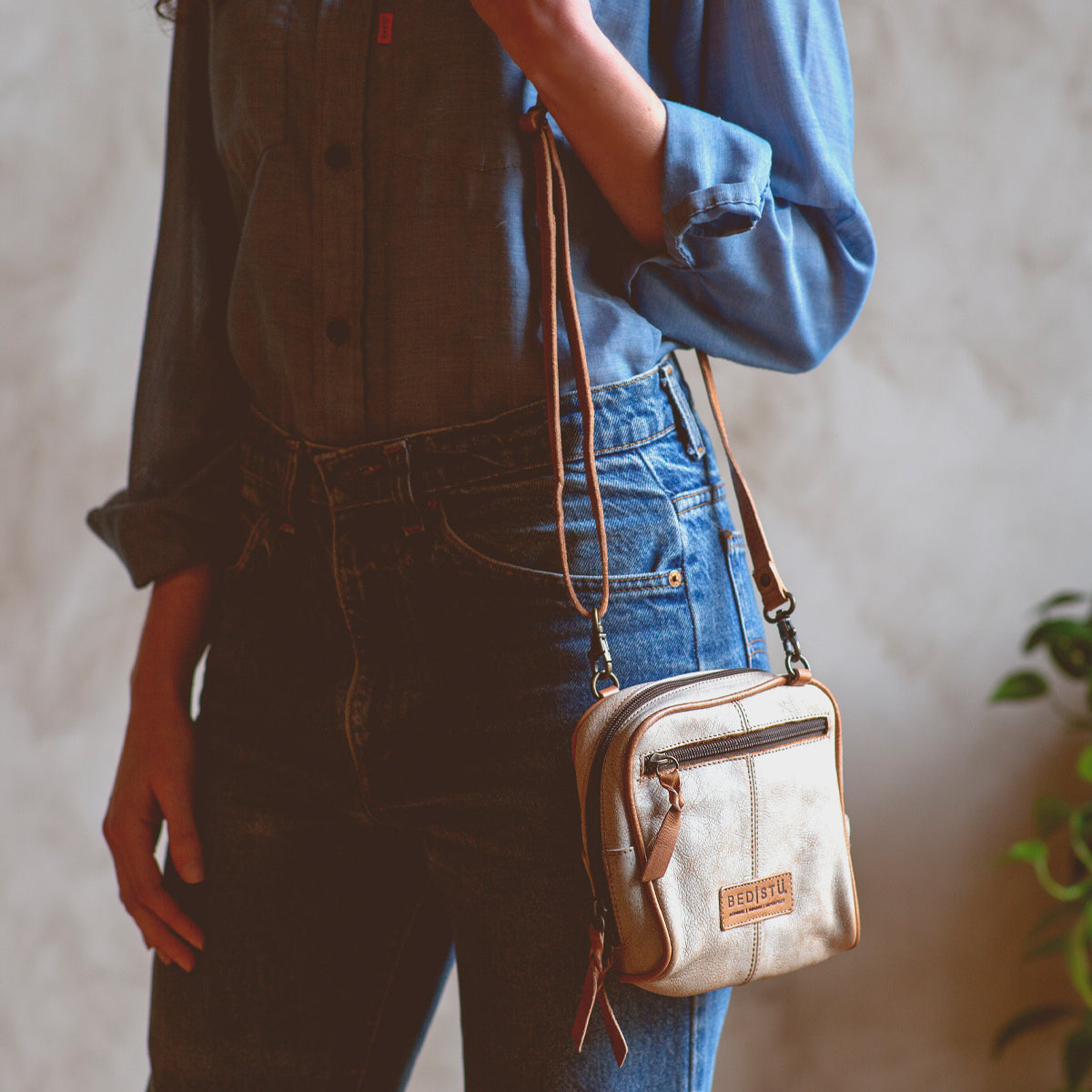 A woman wearing a denim shirt holding a Bed Stu Capture handcrafted cross body bag.