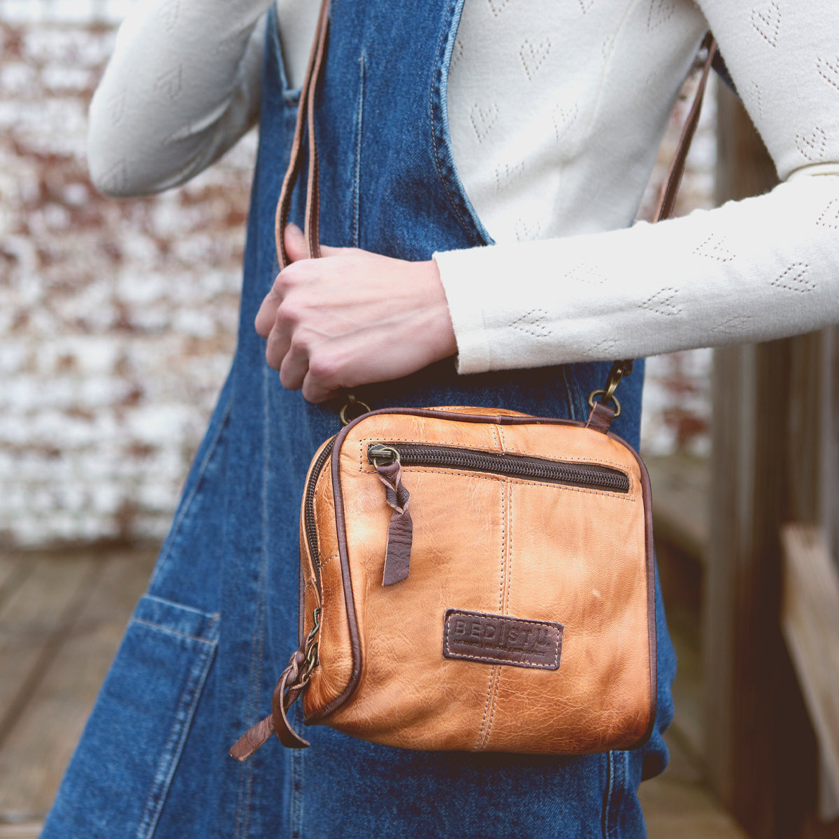 A woman wearing denim overalls holding a Bed Stu Capture cross body bag.