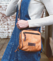 A woman wearing denim overalls holding a Bed Stu Capture cross body bag.