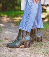 A woman wearing jeans and a pair of green Celestine western-inspired ankle boots from Bed Stu with hem stitch details.
