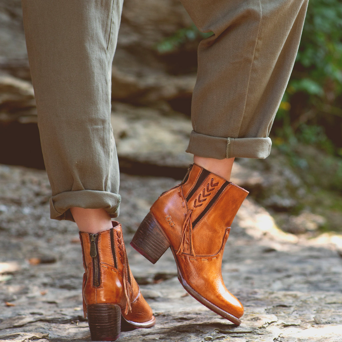 A woman's feet standing on rocks in a pair of Bed Stu Celestine boots.