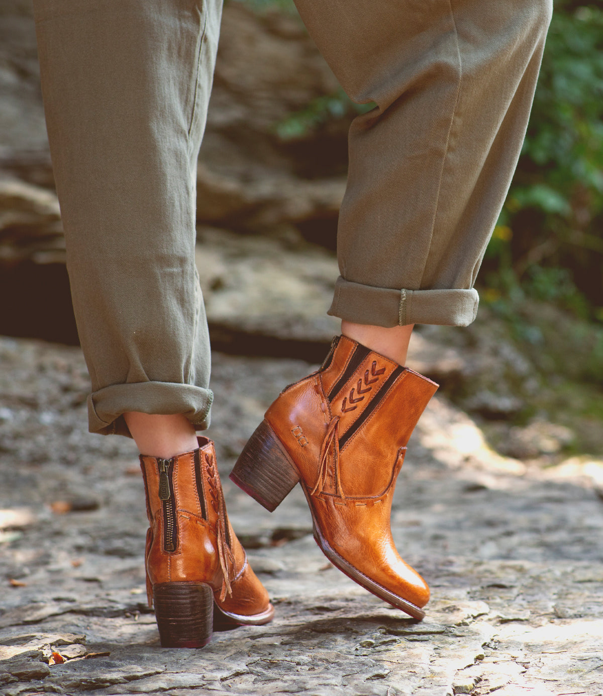 A woman's feet standing on rocks in a pair of Bed Stu Celestine boots.