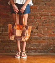 A woman holding a Bed Stu Celindra LTC II leather tote bag in front of a brick wall.